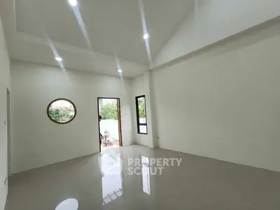 Spacious empty room with modern lighting and unique round window design.