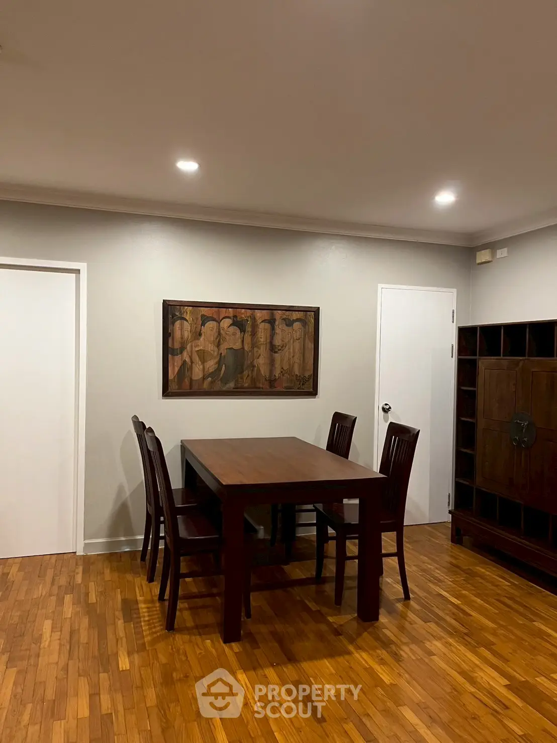Elegant dining area with wooden table and chairs, featuring stylish artwork and warm lighting.