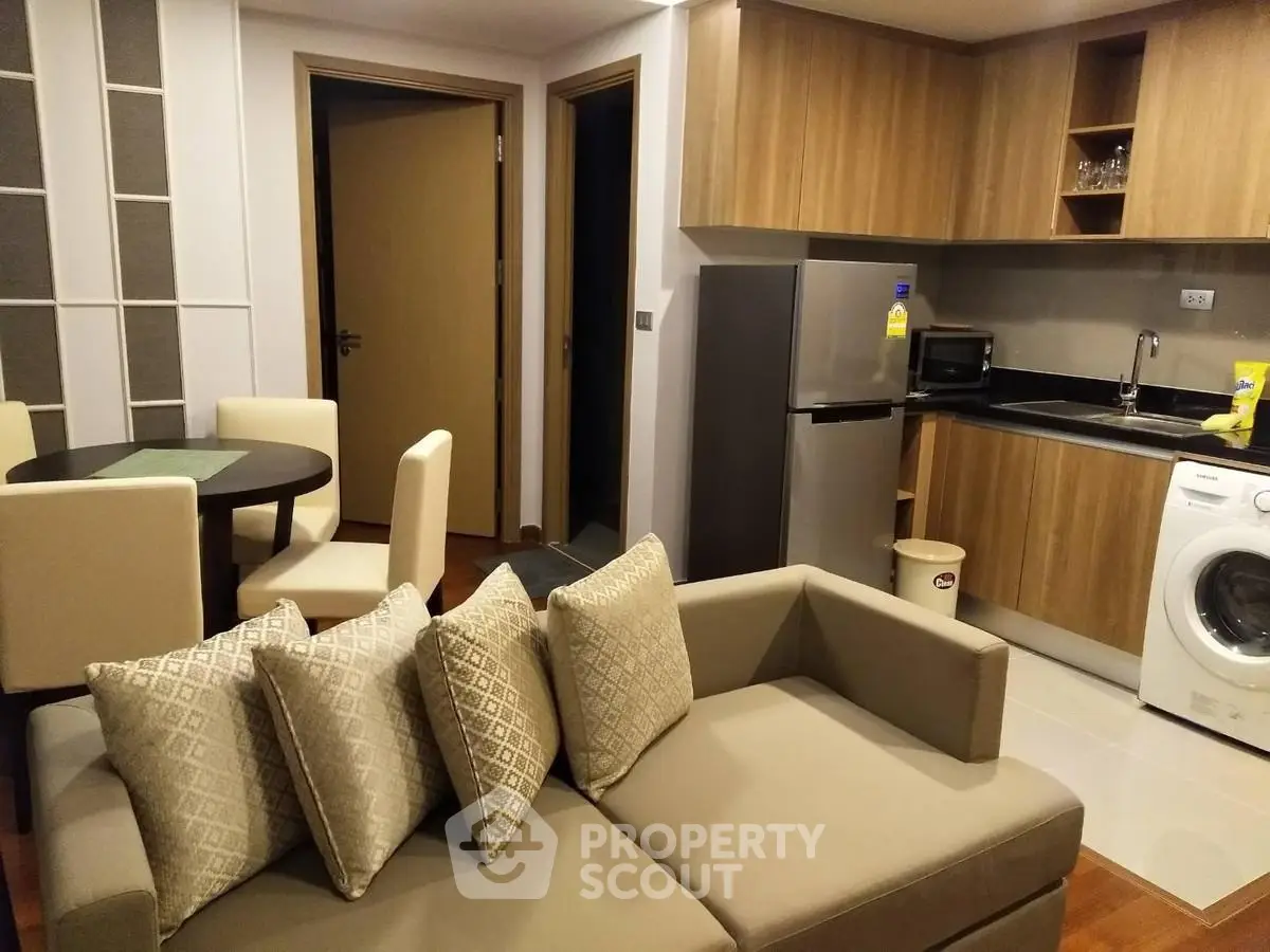 Modern apartment interior with cozy living room and kitchen featuring washing machine and fridge.
