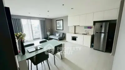 Modern open-plan living room with kitchen and dining area, featuring sleek furniture and large window view.
