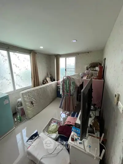 Cluttered bedroom with large windows and floral wallpaper, potential for renovation.