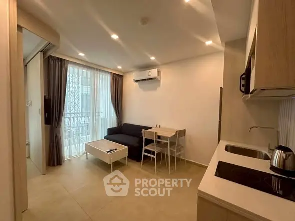 Modern living room with open kitchen, cozy sofa, and dining area in bright apartment.