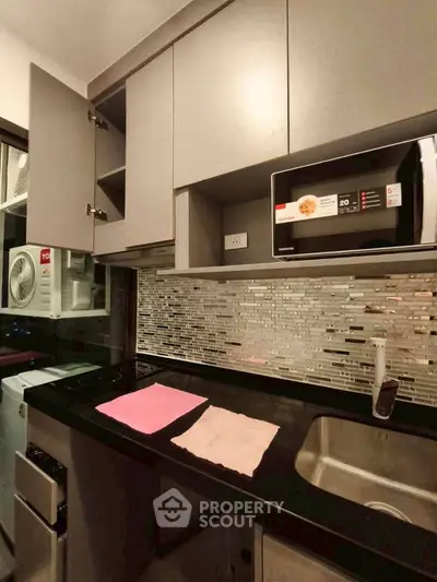 Modern kitchen with sleek cabinetry, microwave, and stylish backsplash in a compact layout.