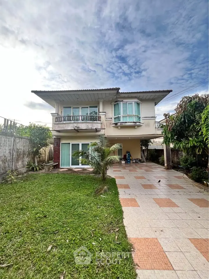 Charming two-story house with spacious garden and tiled patio under a clear blue sky.