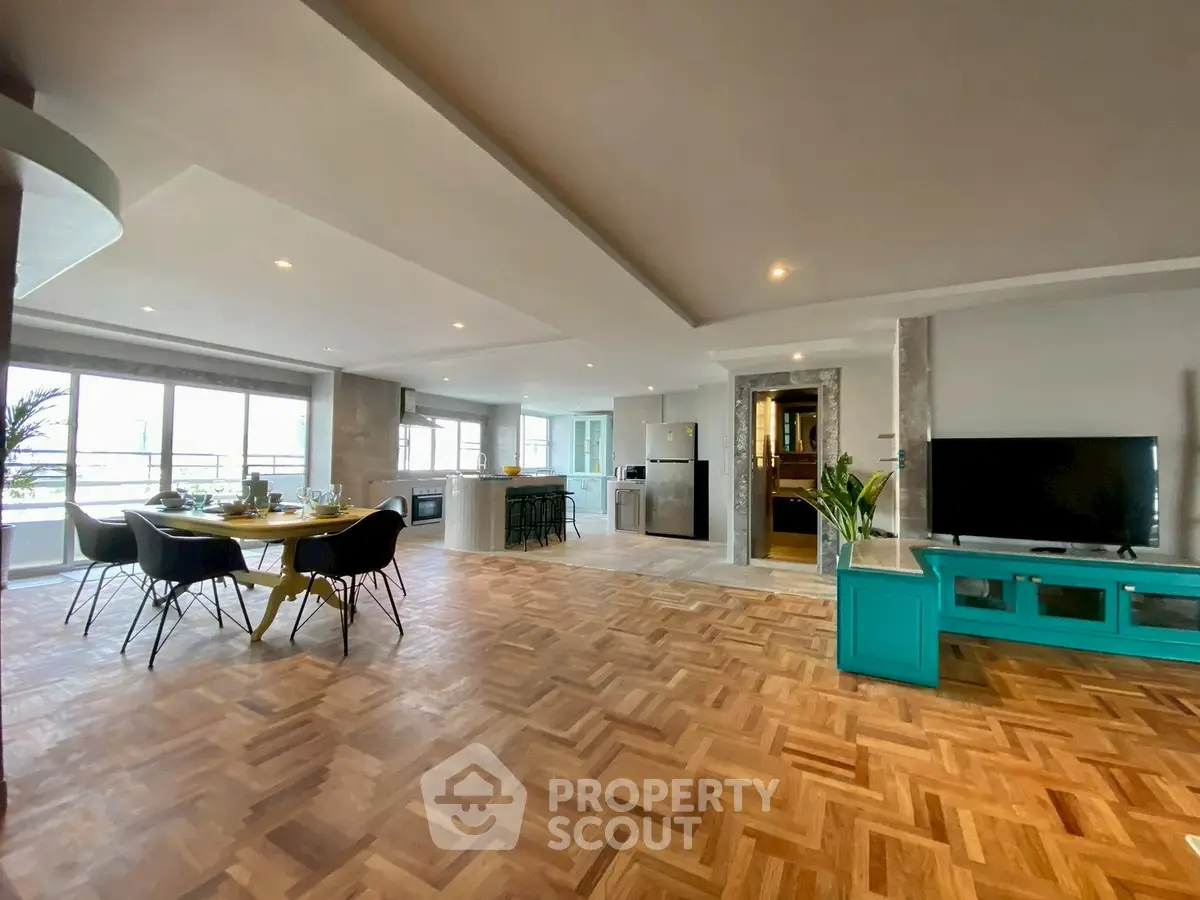 Spacious open-plan living room with dining area and modern kitchen, featuring parquet flooring and large windows.