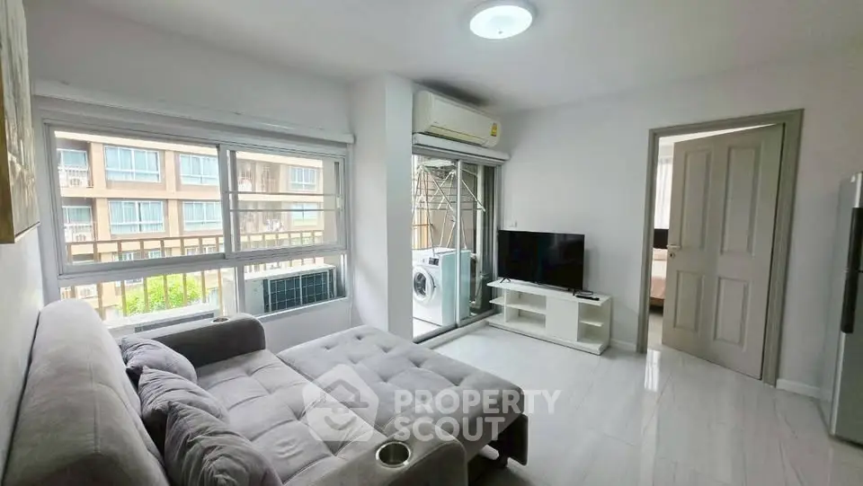 Modern living room with gray sofa, TV, and large windows in a bright apartment.