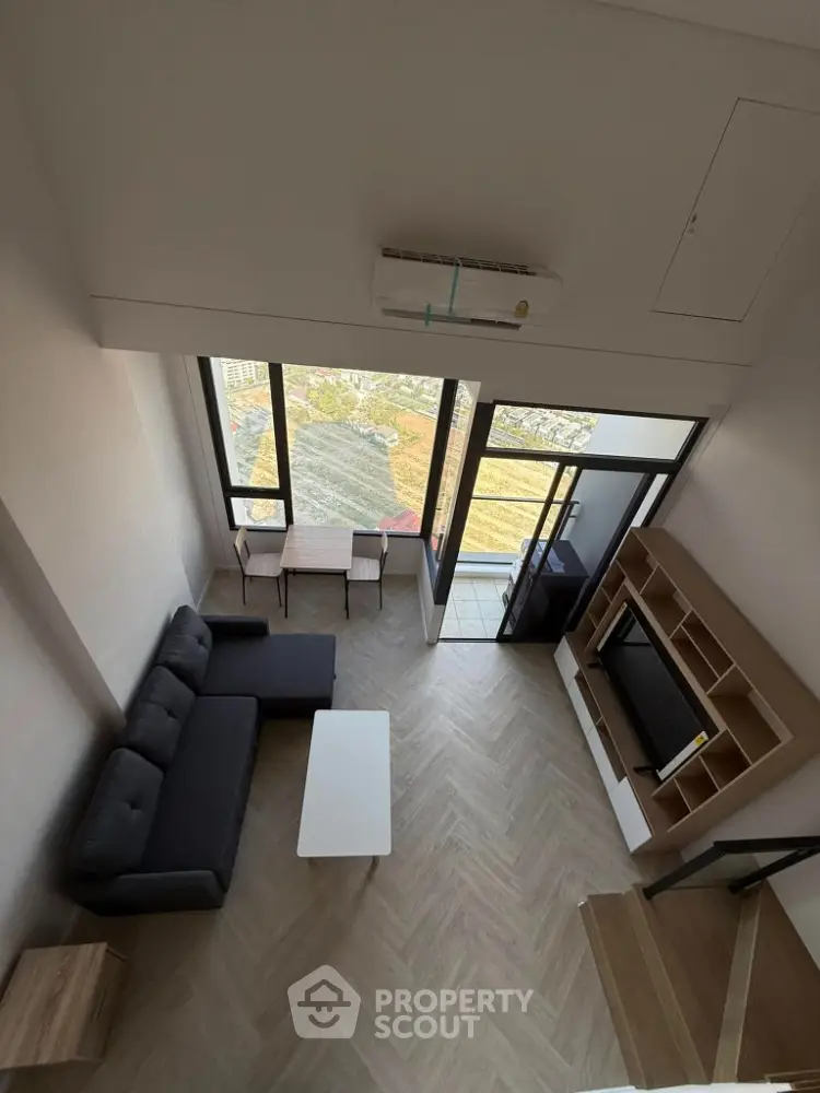Modern loft-style living room with high ceiling and large windows offering city views.