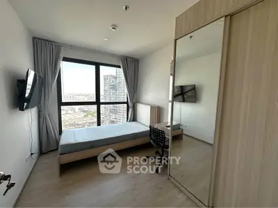 Modern bedroom with large window and city view, featuring a bed, desk, and wall-mounted TV.