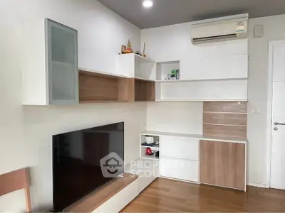 Modern living room with sleek built-in storage and flat-screen TV, featuring wooden flooring and air conditioning.