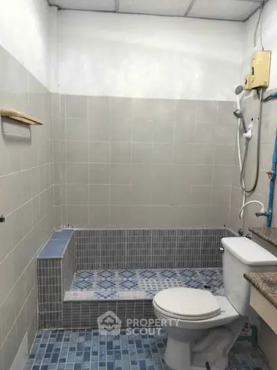 Compact bathroom with tiled shower area and toilet, featuring neutral tones and practical design.