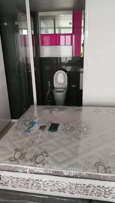 Compact bedroom with attached bathroom featuring modern fixtures and a new mattress.