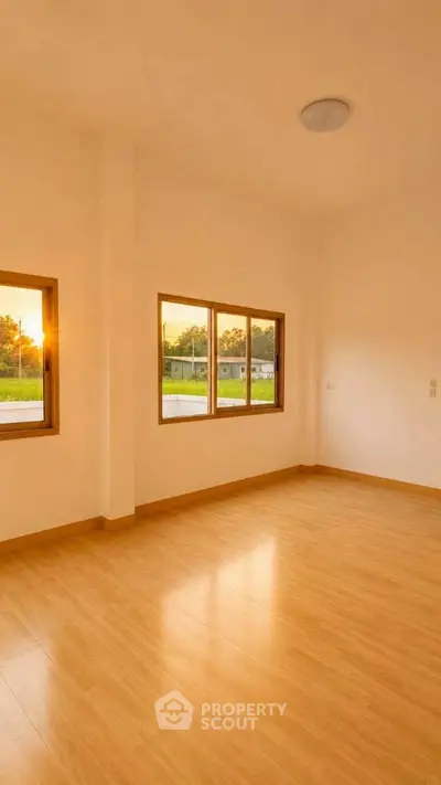 Spacious empty room with large windows and wooden flooring, offering a serene view of the outdoors.