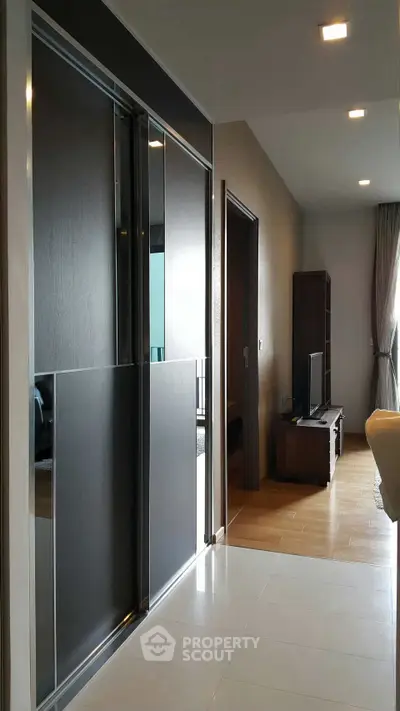 Modern apartment hallway leading to a cozy living room with sleek furniture and natural lighting.