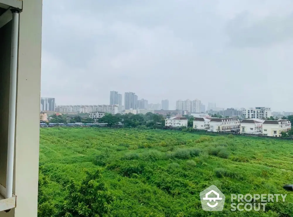 Stunning cityscape view from a high-rise apartment overlooking lush green fields and urban skyline.