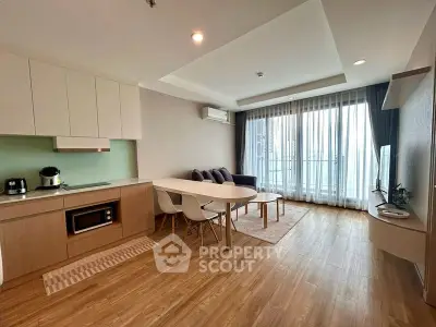 Modern open-layout living room with kitchen, featuring sleek furniture and large windows for natural light.