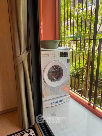 Modern apartment balcony with Samsung washing machine and lush greenery view.
