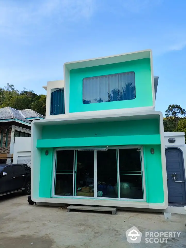 Modern two-story turquoise house with large windows and sliding glass doors