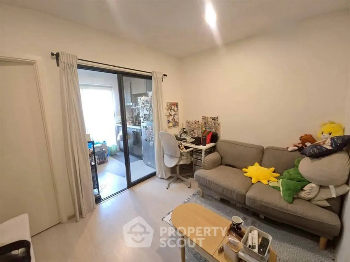 Cozy living room with sliding glass door to balcony, featuring a comfortable sofa and a study desk.