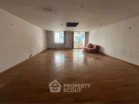 Spacious empty living room with wooden flooring and large windows.