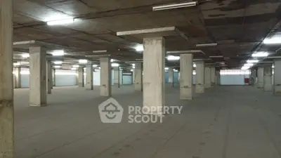 Spacious industrial warehouse with concrete pillars and high ceilings, ideal for storage or manufacturing.