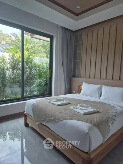 Luxurious bedroom with large window and garden view, featuring elegant decor and cozy bedding.
