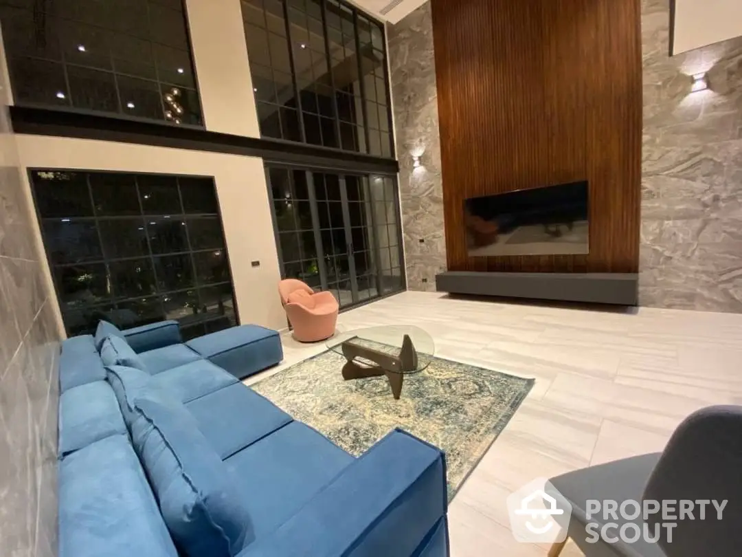 Luxurious living room with high ceilings, expansive windows, and a modern fireplace, complemented by a plush blue sofa and elegant marble walls.