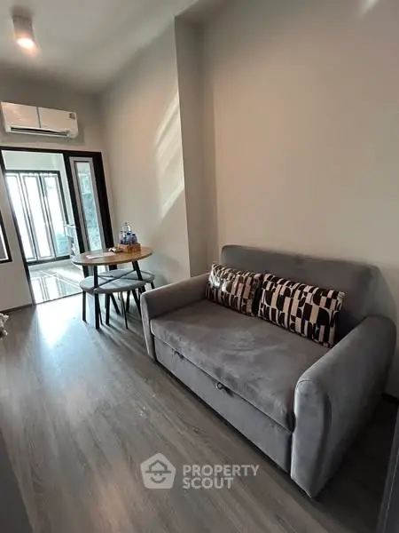 Modern living room with gray sofa and dining table, featuring sleek flooring and air conditioning.