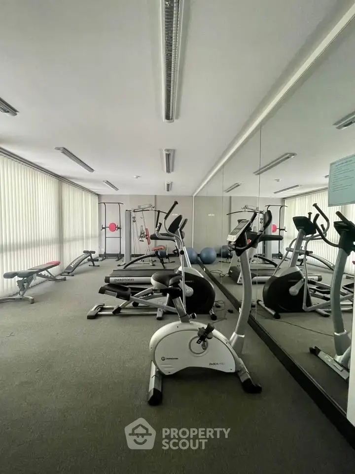 Spacious gym with modern exercise equipment and mirrored walls in a residential building.