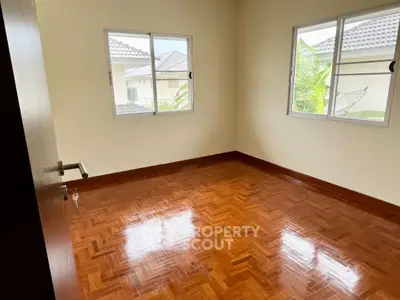 Spacious bedroom with polished wooden floors and large windows offering natural light.