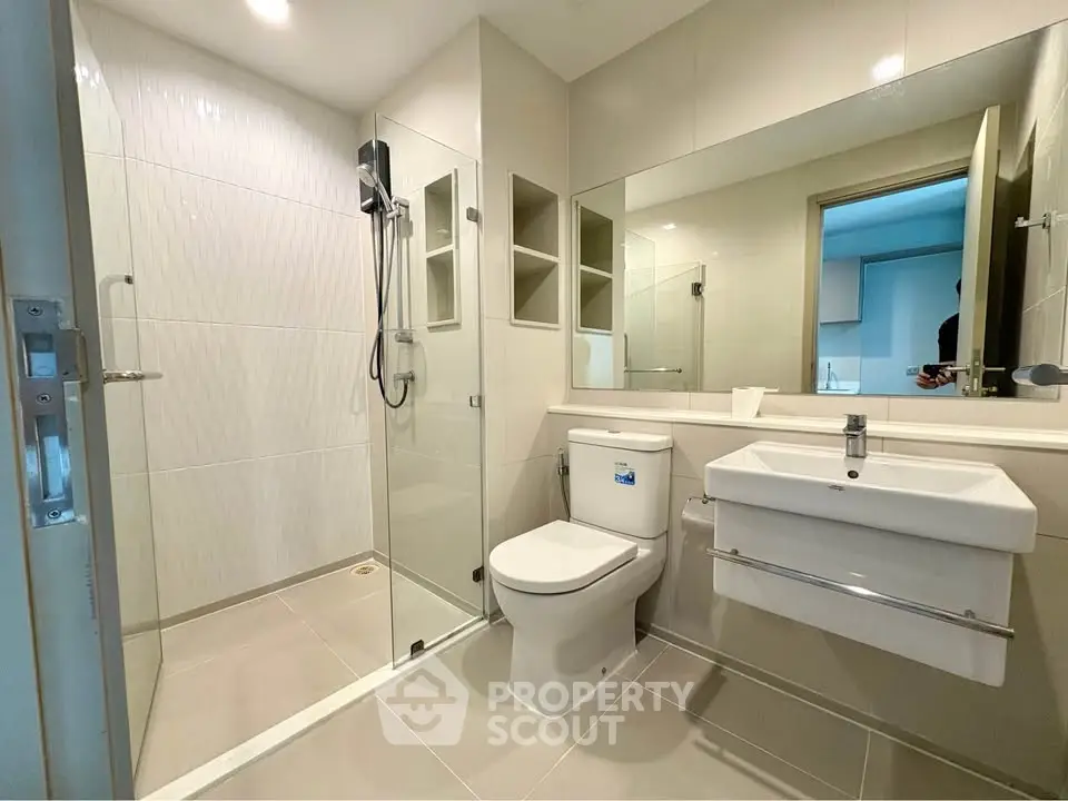 Modern bathroom with glass shower, sleek fixtures, and large mirror in a contemporary apartment.
