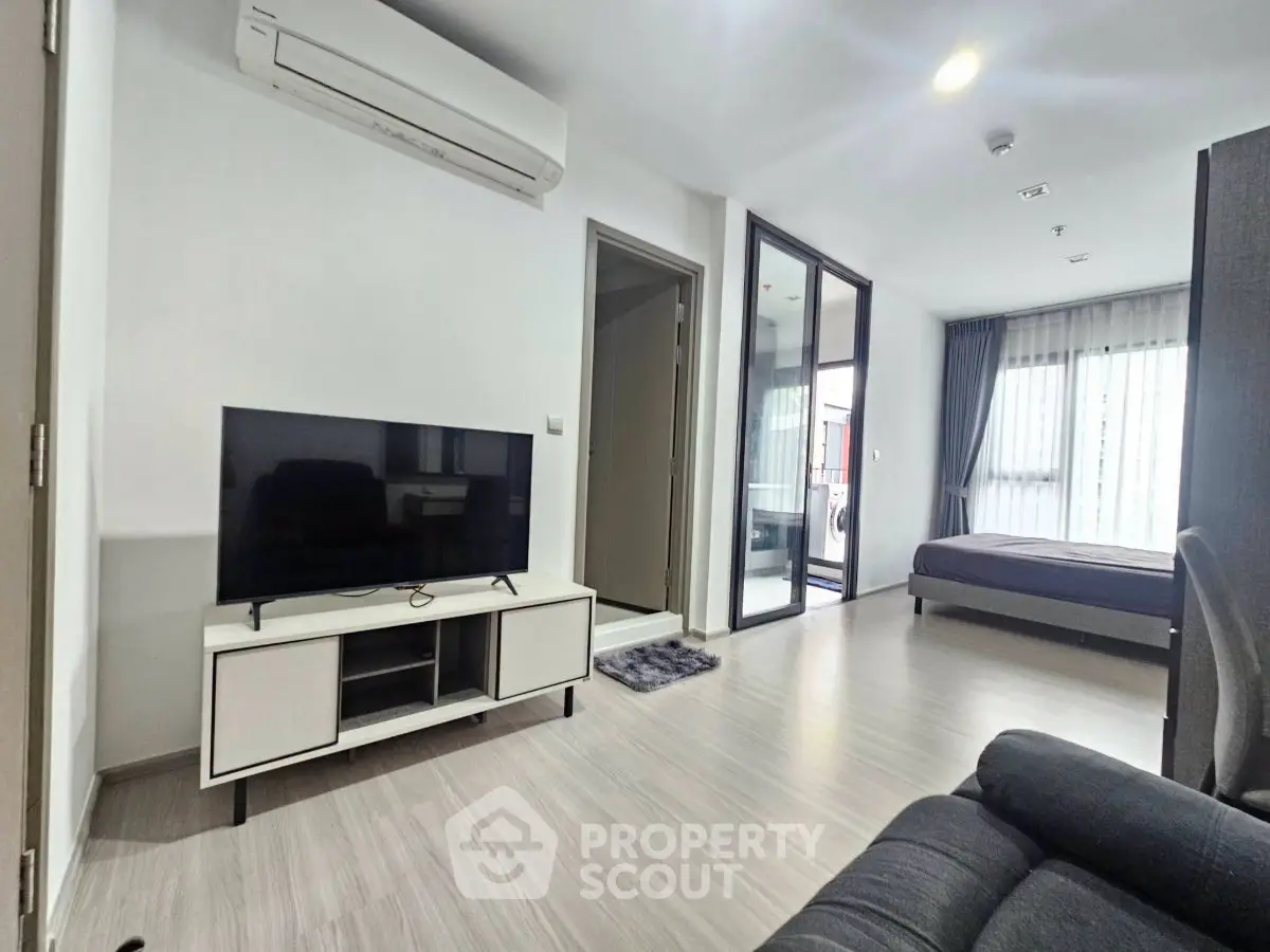 Modern open-plan living room with TV and air conditioning, leading to a cozy bedroom.