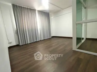 Spacious empty room with wooden flooring and large window, ideal for customization.