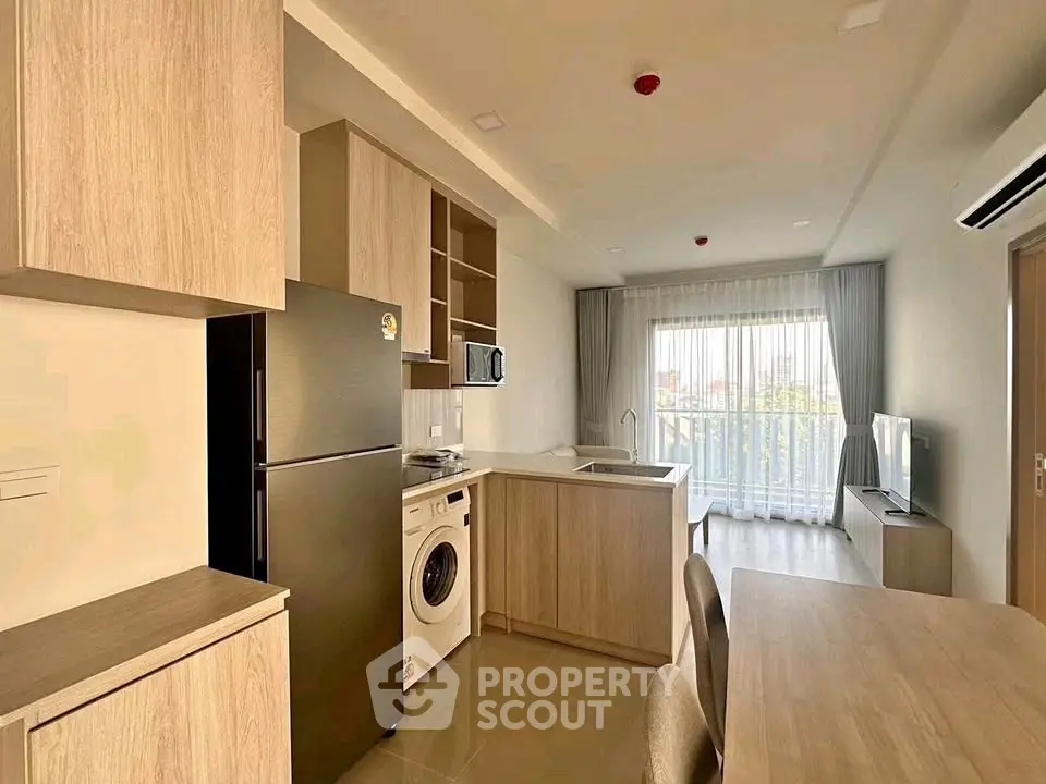 Modern open-layout kitchen with appliances and bright living area leading to a balcony.