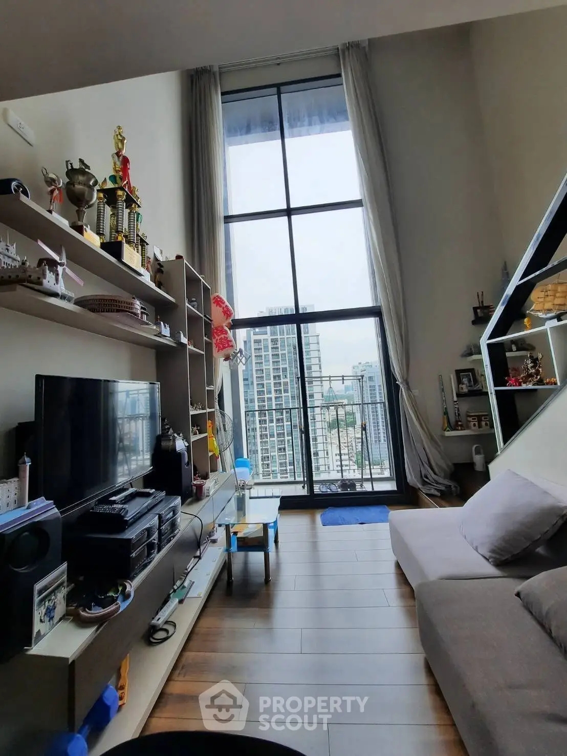 Modern living room with high ceilings and city view, featuring stylish decor and entertainment setup.