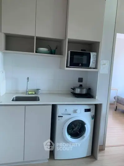 Modern compact kitchen with washing machine and microwave in a cozy apartment.