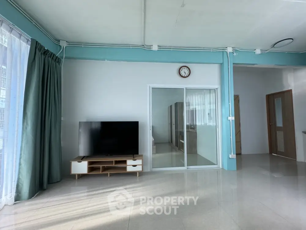 Spacious living room with modern TV setup and large windows for natural light.