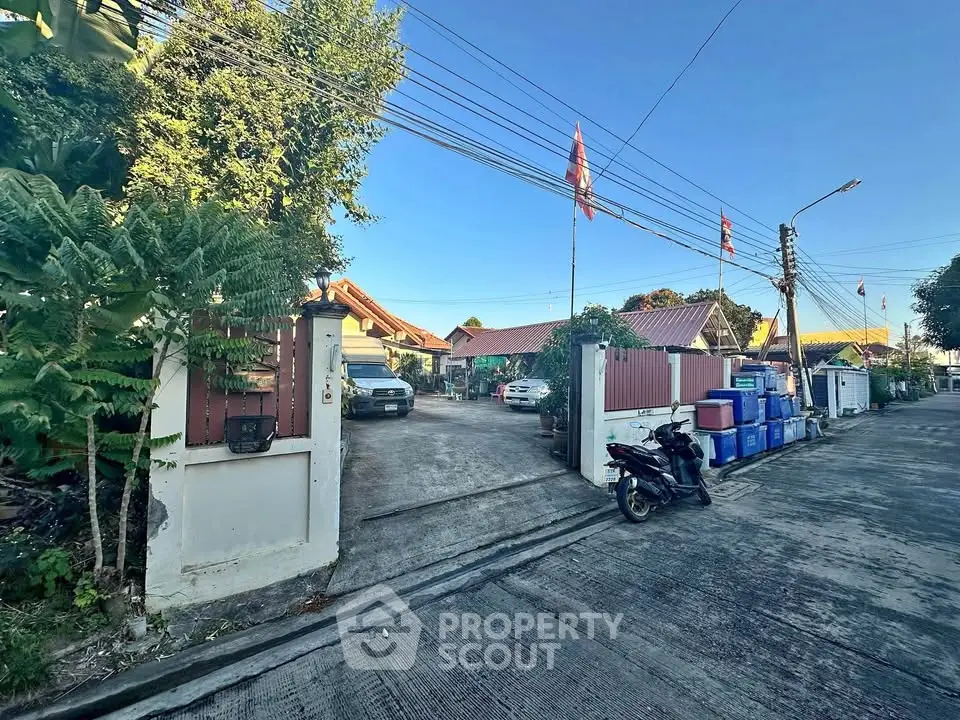 Charming residential entrance with lush greenery and parked vehicles in a serene neighborhood.