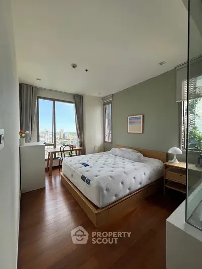 Spacious bedroom with large window offering stunning city views, modern decor, and wooden flooring.