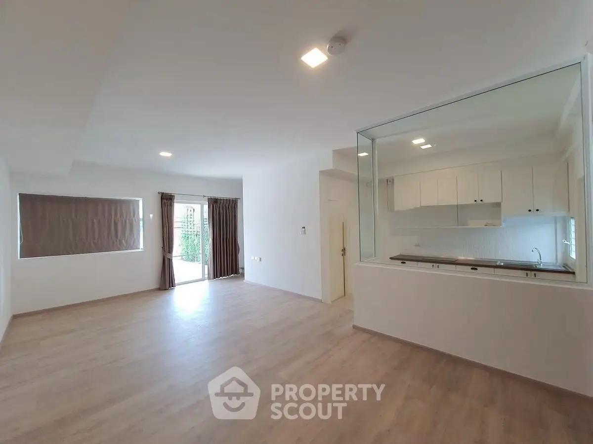 Spacious open-plan living room with large windows and modern kitchen view.