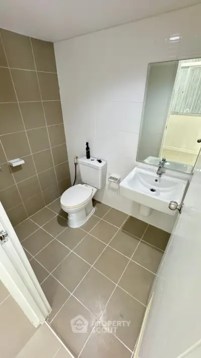 Modern bathroom with sleek design and neutral tiles, featuring a compact layout and contemporary fixtures.