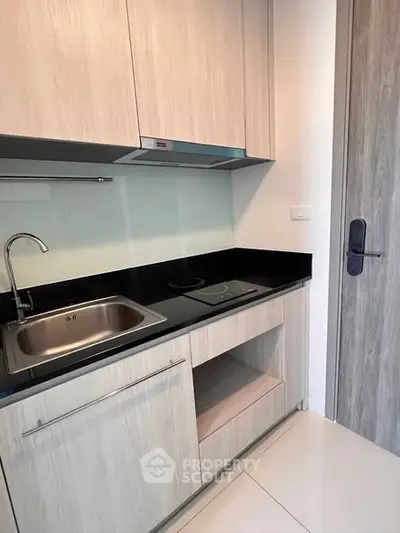 Modern compact kitchen with sleek cabinetry and electric cooktop in a stylish apartment.