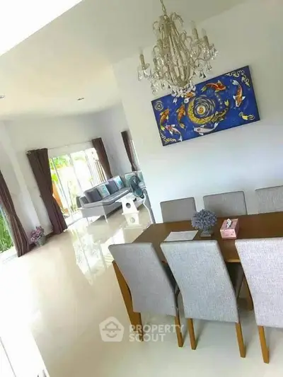 Elegant dining area with chandelier and modern art, open layout leading to spacious living room with natural light.