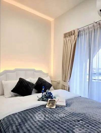 Cozy bedroom with elegant decor and natural light through large window.