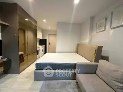 Modern studio apartment with sleek design, featuring a cozy bed, mirrored wardrobe, and compact kitchen area.