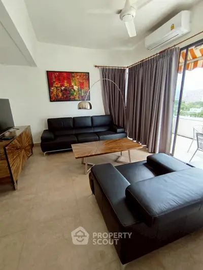Modern living room with sleek black leather sofas, stylish wooden furniture, and a balcony view.