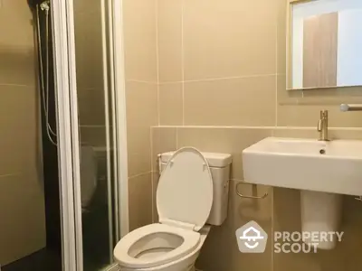 Compact modern bathroom with beige tiles, featuring a wall-mounted sink, toilet, and shower with glass door, ideal for urban living.