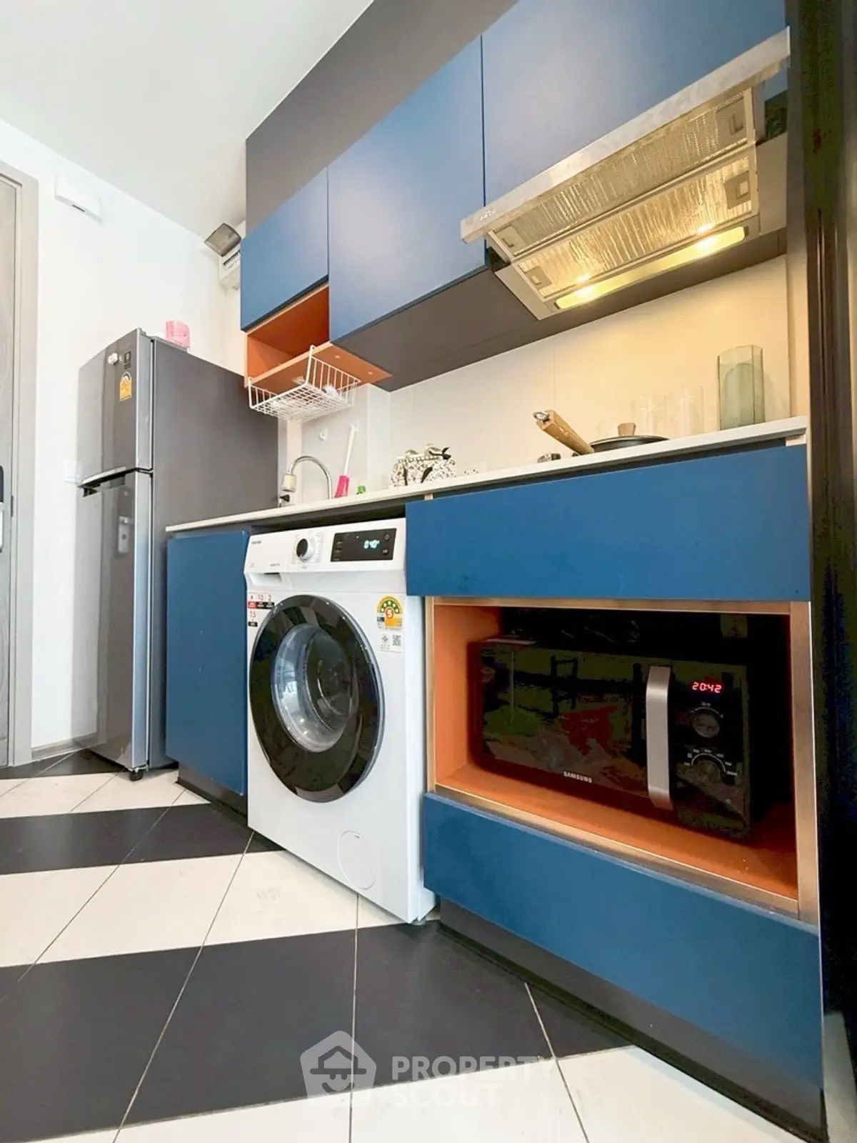 Modern kitchen with blue cabinets, washing machine, and microwave in stylish apartment.