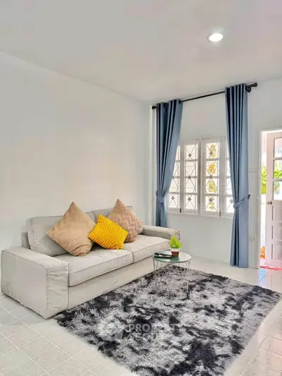 Cozy living room with modern decor, featuring a plush sofa, stylish rug, and natural light from large windows.