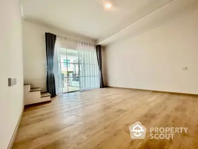 Spacious empty room with wooden flooring and balcony access