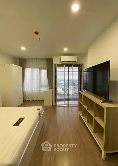 Modern bedroom with large window and balcony access, featuring sleek wooden flooring and contemporary furniture.